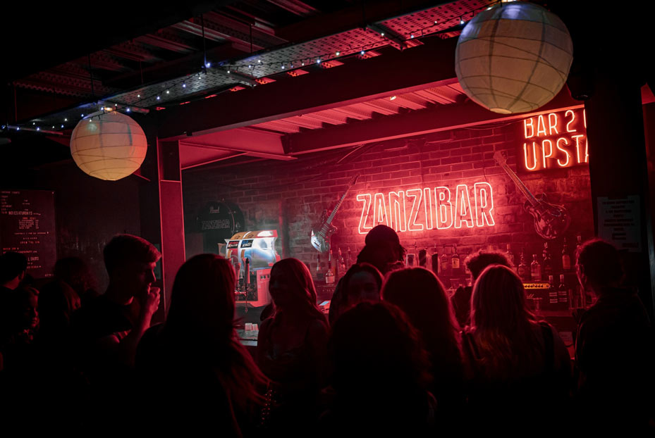 People queuing up at the Zanzibar bar area for drinks with neon lights reflecting on their faces